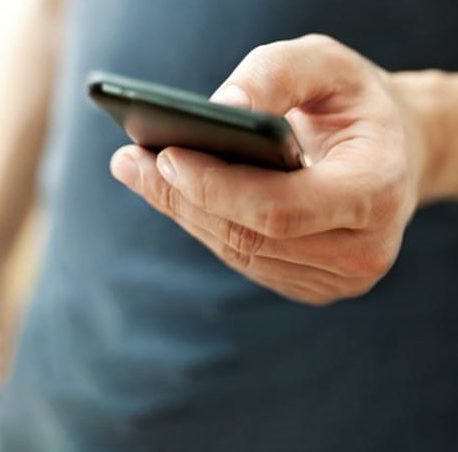 Zahlungsmittel: Großaufnahme einer linken Hand, die ein Smartphone hält und mit dem Daumen darauf tippt.
